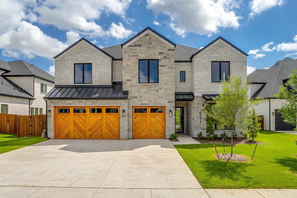 Two-story stone custom home with cedar garage doors and a standing seam metal porch roof
