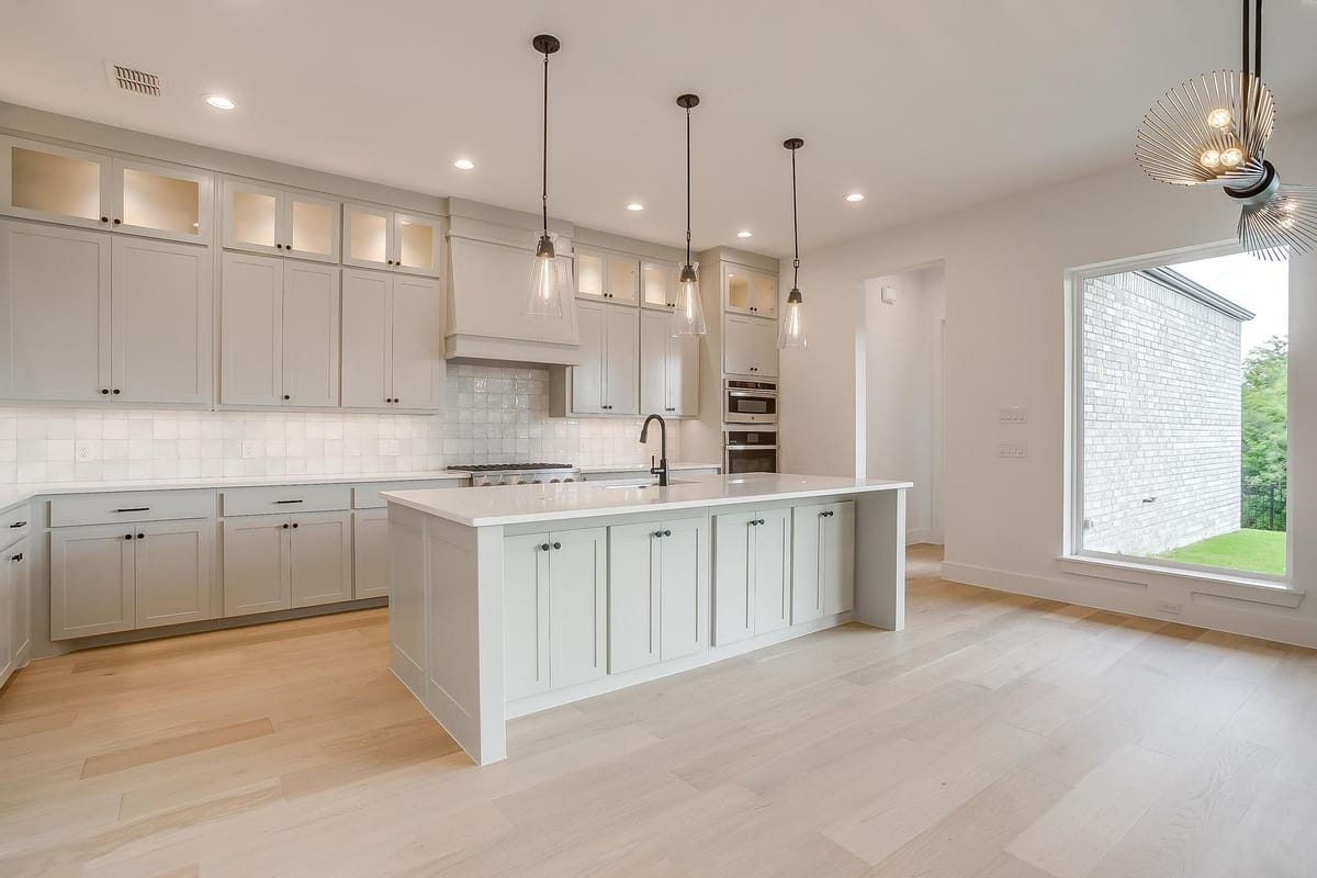 Kitchen with a long island, pendant lights, and a run of wall ovens