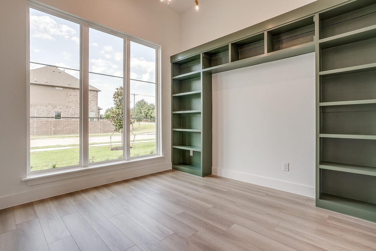 Study with built-in shelving painted deep green beside a window wall